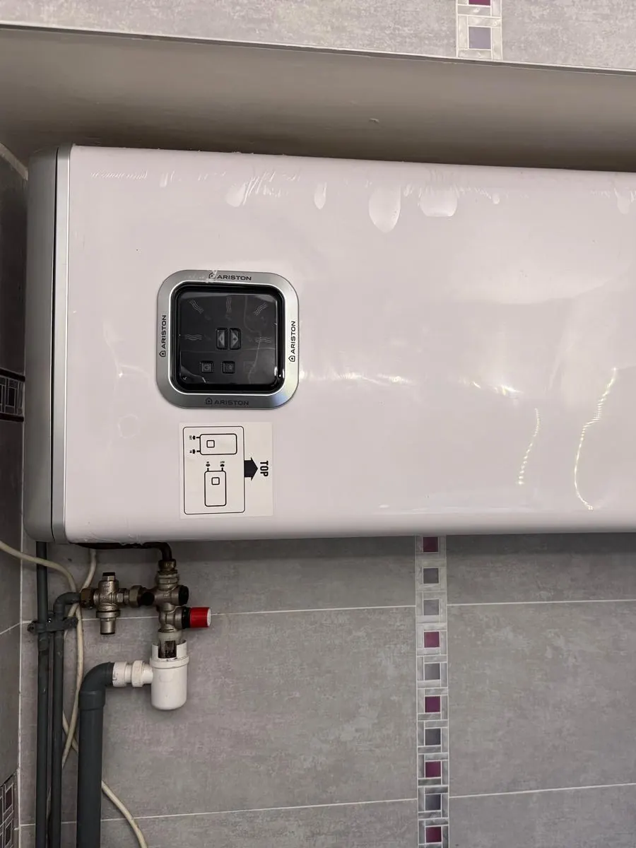 Chauffe-eau plat Ariston posé à l’horizontale sous un coffrage de salle de bains, groupe de sécurité en dessous